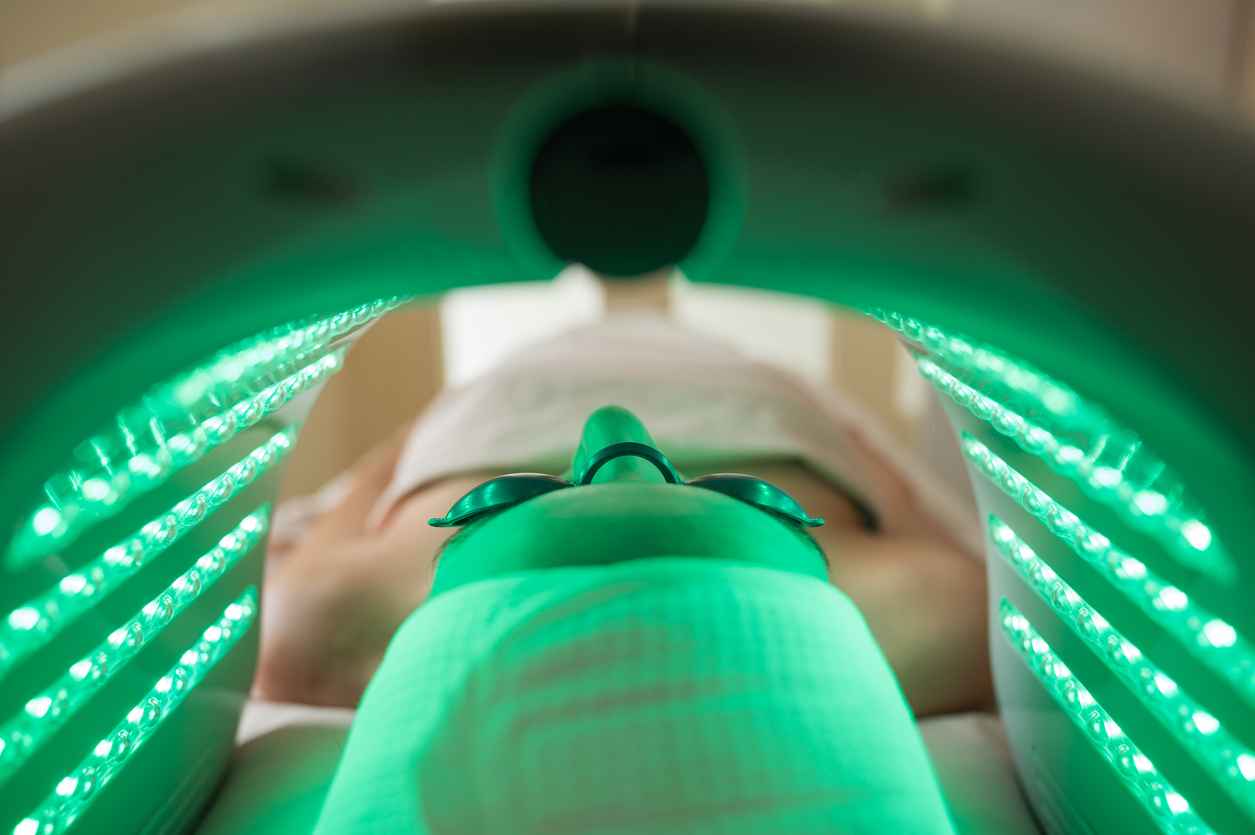 Woman lying down and wearing eye protection during a rejuvenating LED green light therapy session at a beauty salon, enhancing her skincare routine